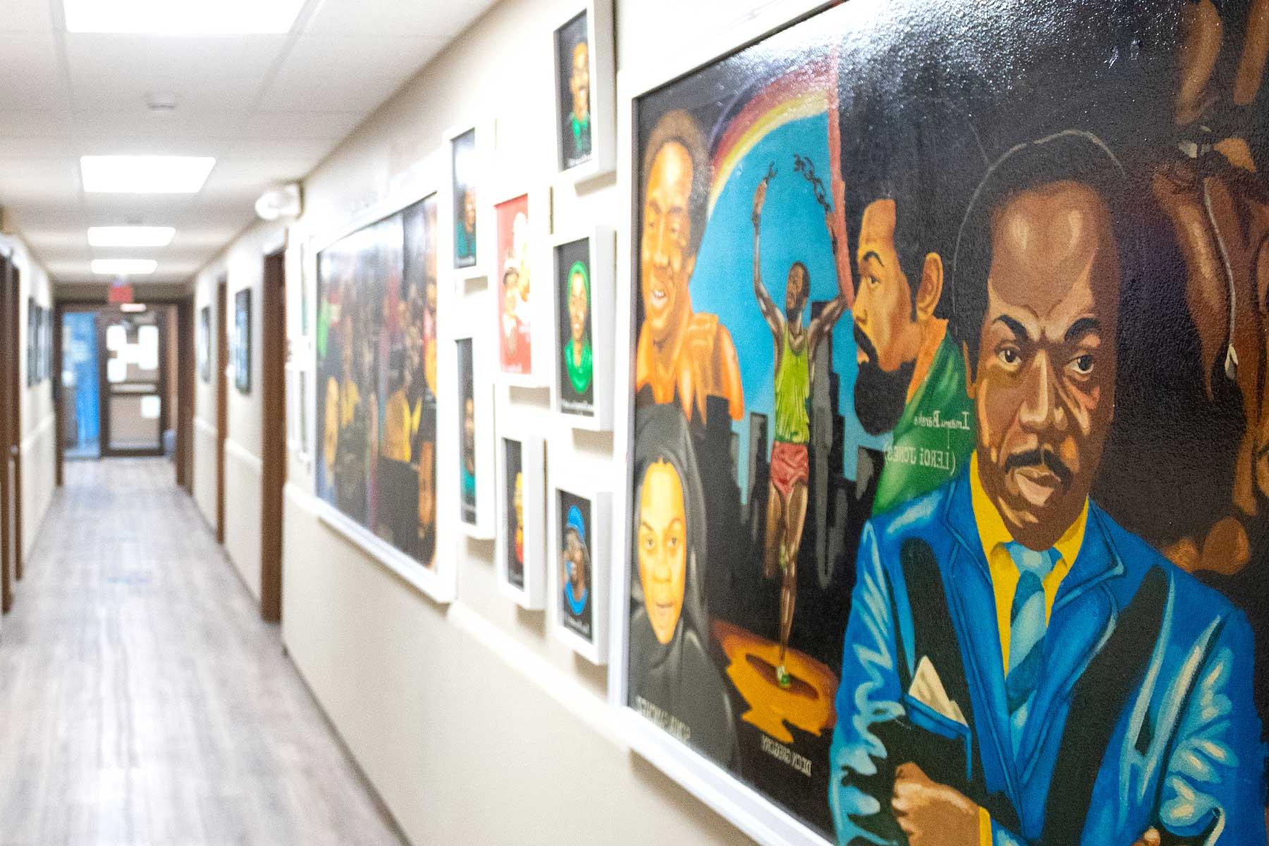 A hallway with a variety of picture frames on the wall. The frames feature colorful artwork of historic Black activists and known personalities.